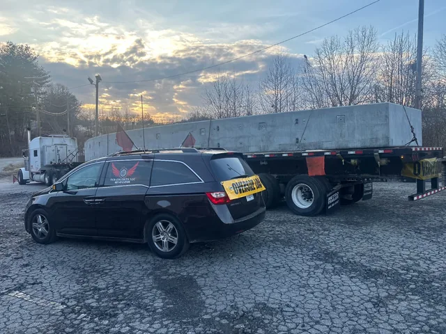 TCB Escorts pilot car with an oversize load sign beside a flatbed carrying a precast concrete section