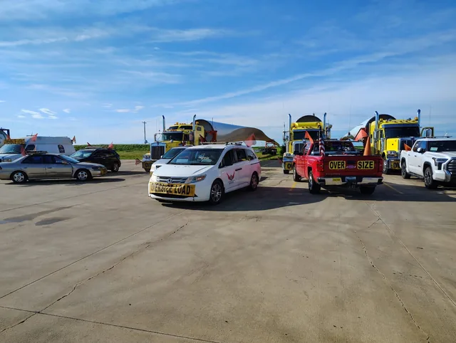 TCB Escorts pilot cars with oversize load signs lined up beside trucks hauling wind turbine blades