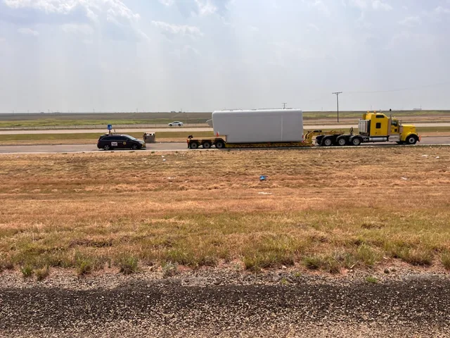 TCB Escorts pilot car traveling ahead of a truck hauling an oversize load on a divided highway
